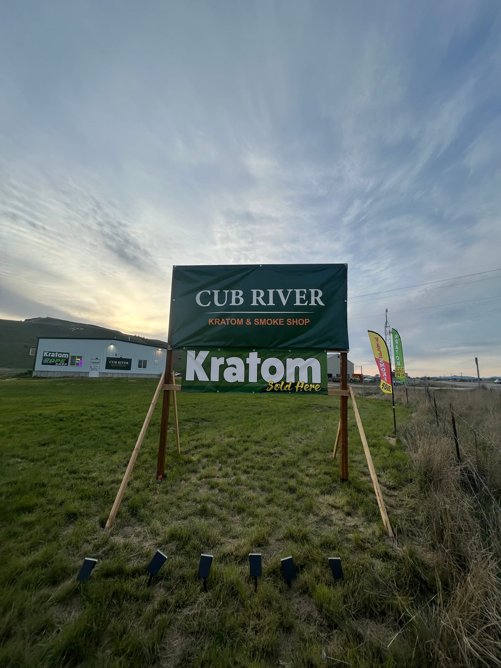 Cub River Kratom & Smoke Shop storefront sign reading "Kratom Sold Here" against an evening sky